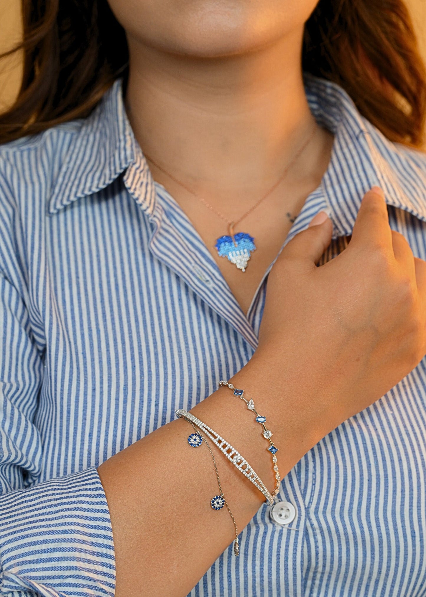 Person wearing a blue heart-shaped pendant necklace and multiple bracelets on a striped shirt background