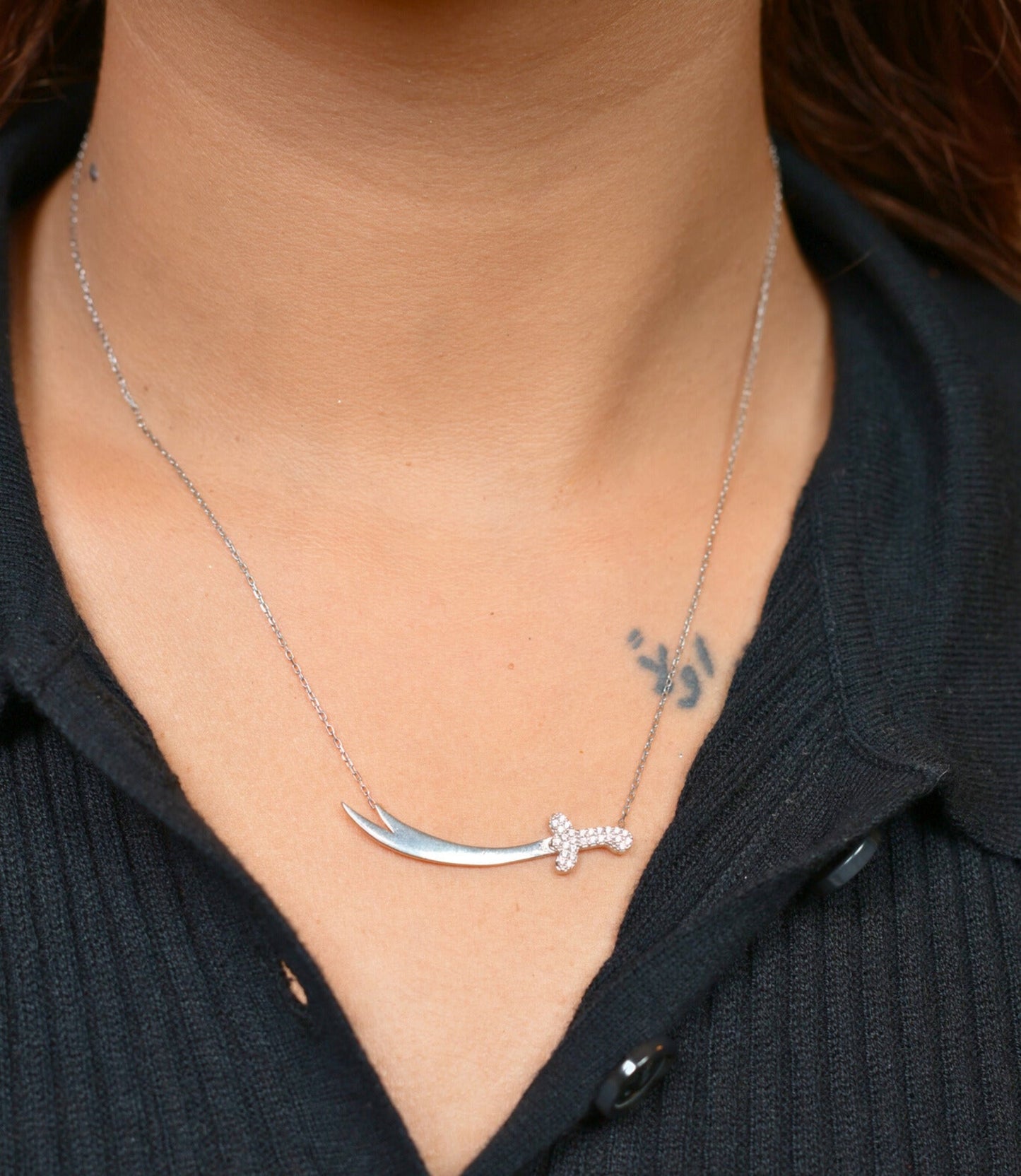 Silver necklace with a unique pendant worn by a person against a black shirt background