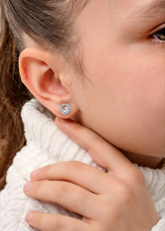 Close-up of a person wearing a silver earring with a clear gemstone.