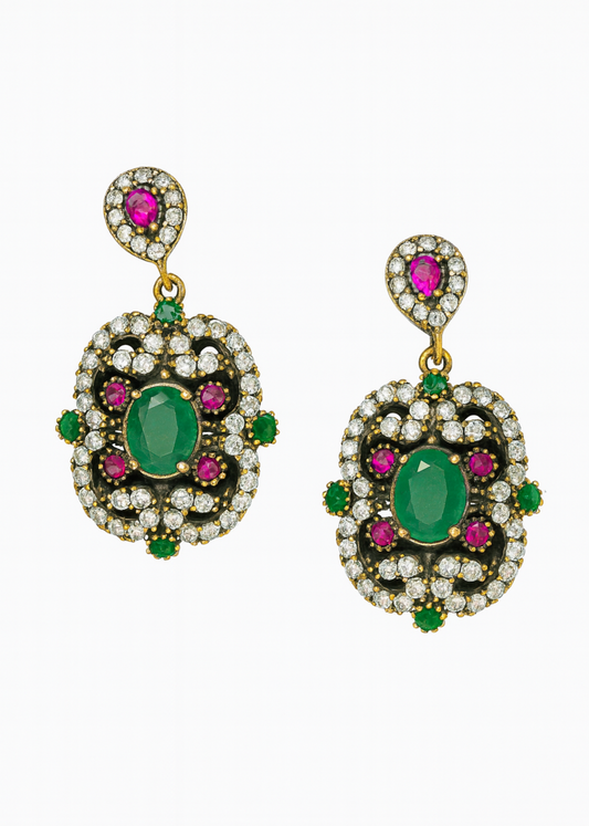 Pair of ornate earrings with green and pink gemstones on a white background