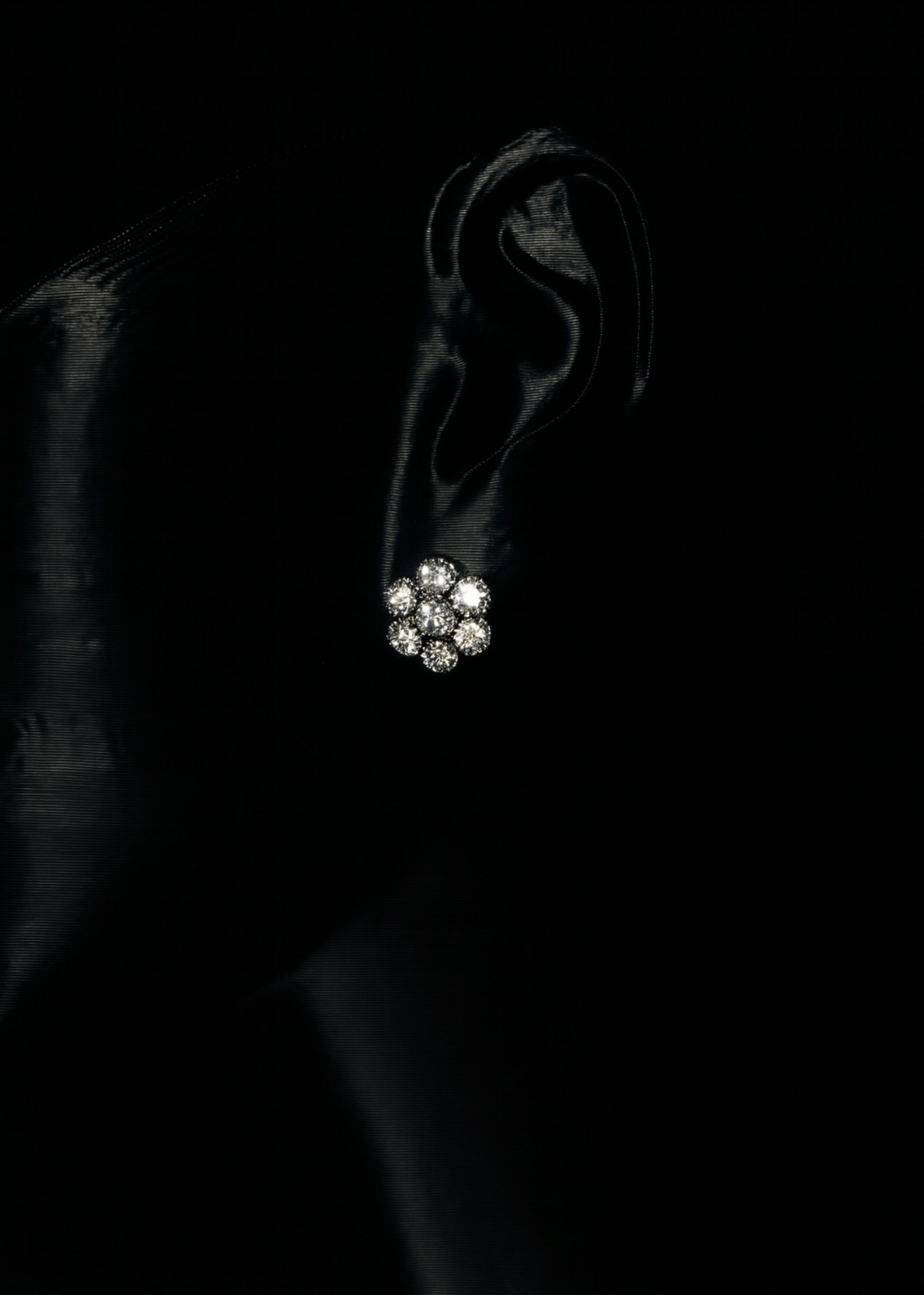Close-up of an ear wearing a diamond earring against a black background