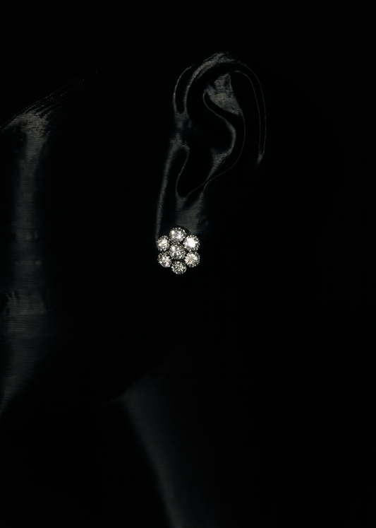 Close-up of an ear wearing a diamond earring against a black background
