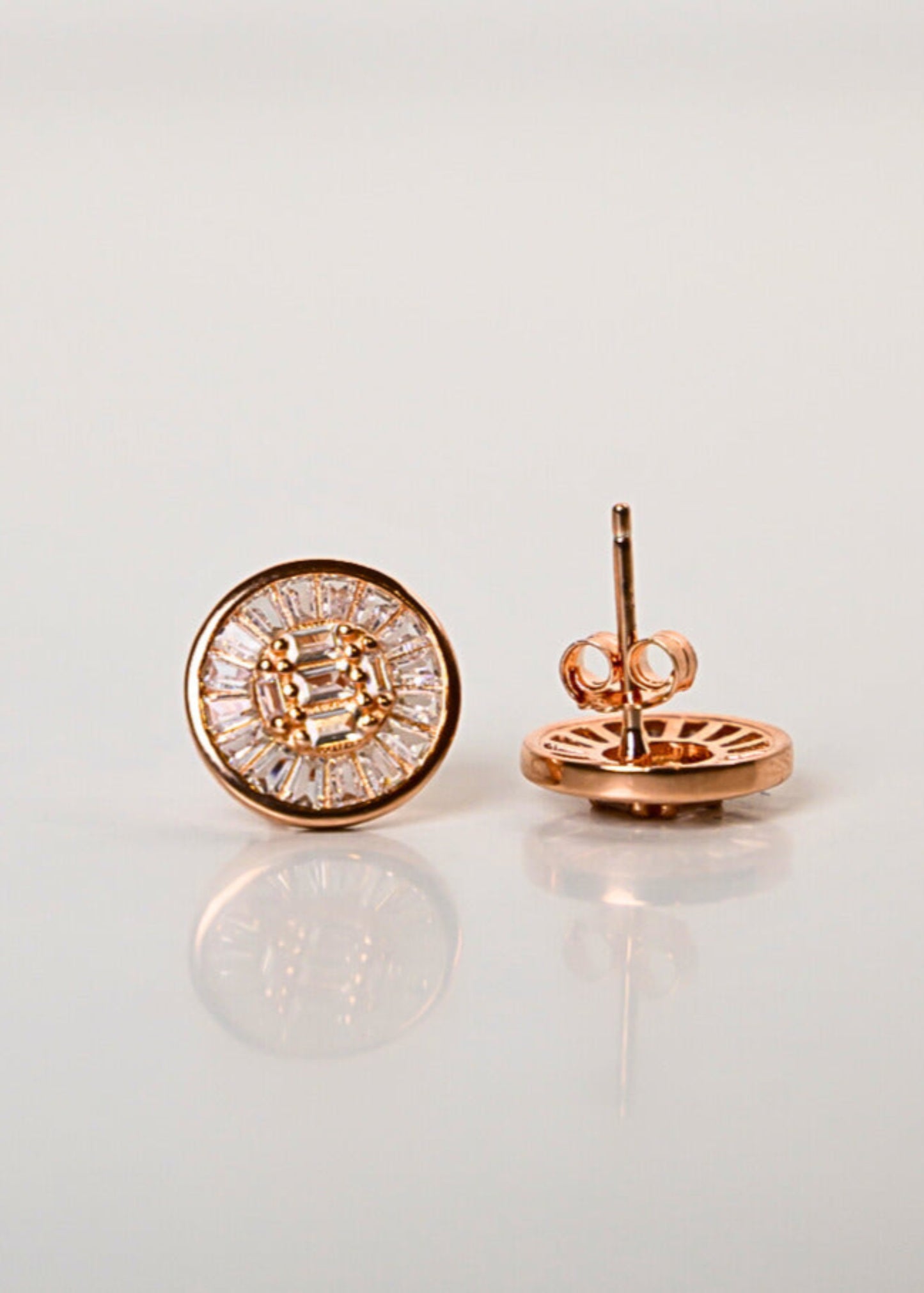 Rose gold earrings with clear gemstones on a light gray background