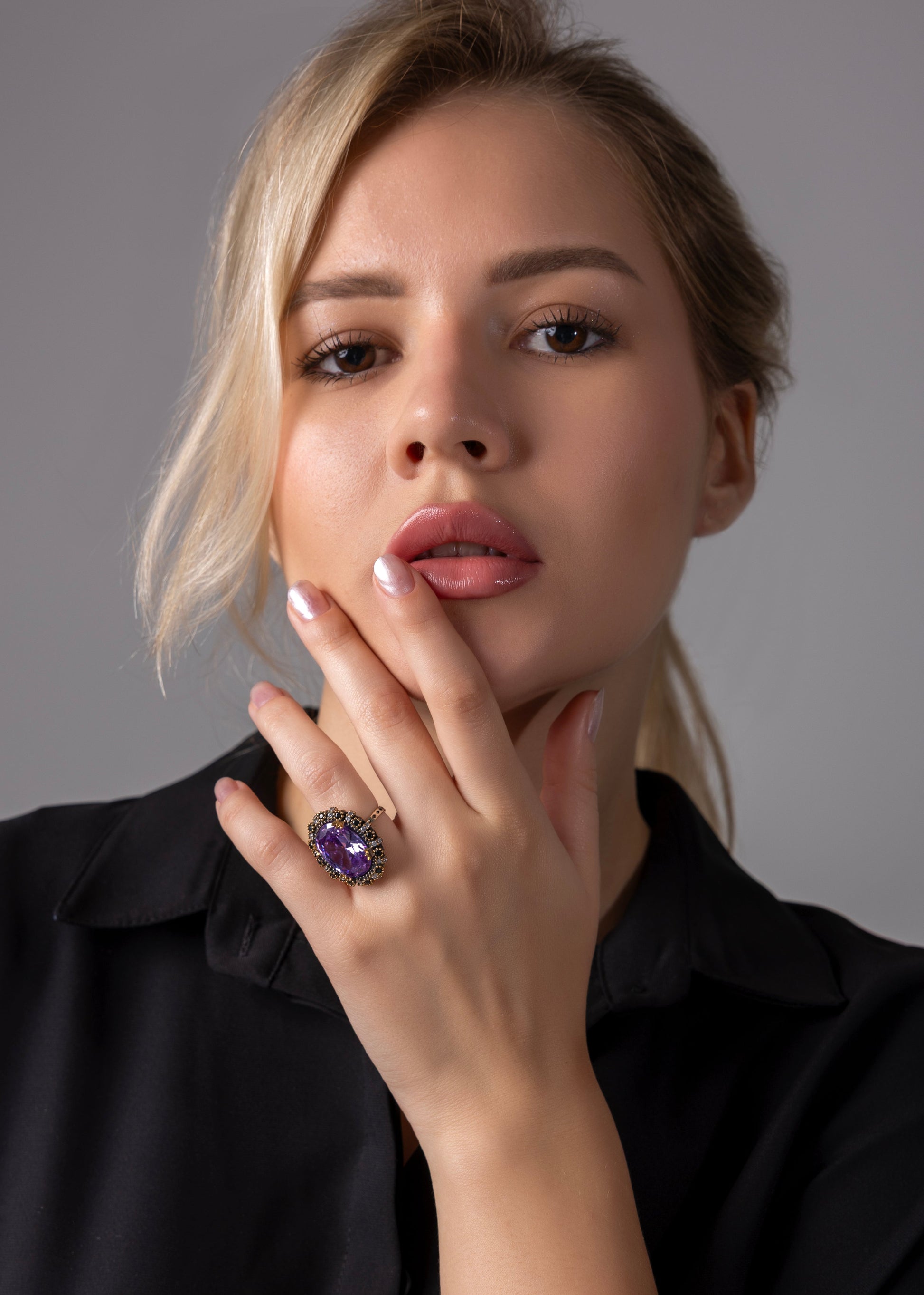 Woman wearing a black shirt with a hand resting on her chin, featuring a purple gemstone ring.