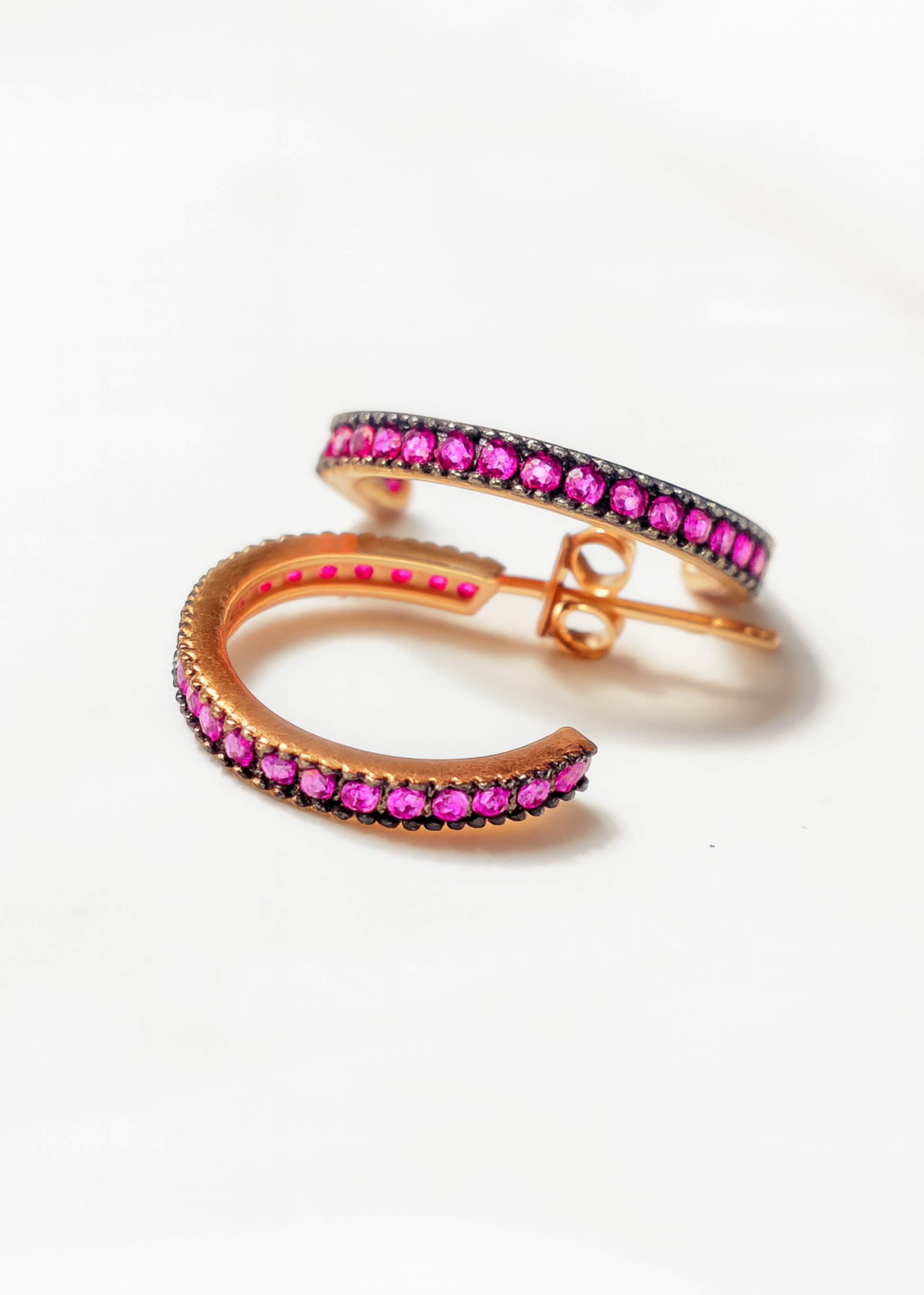 Pair of gold hoop earrings with pink gemstones on a white background