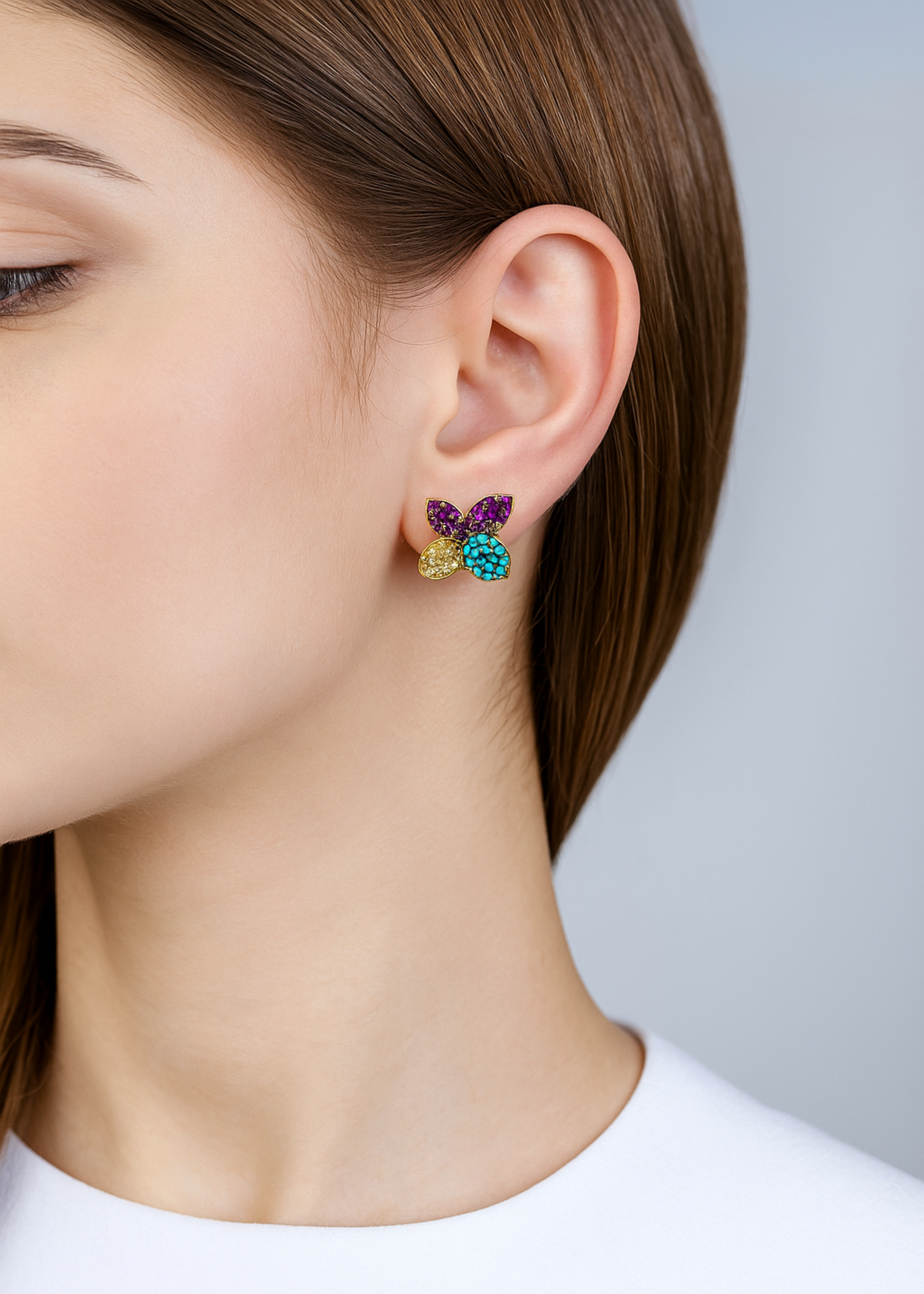Multicolored earrings worn by a person against a neutral background