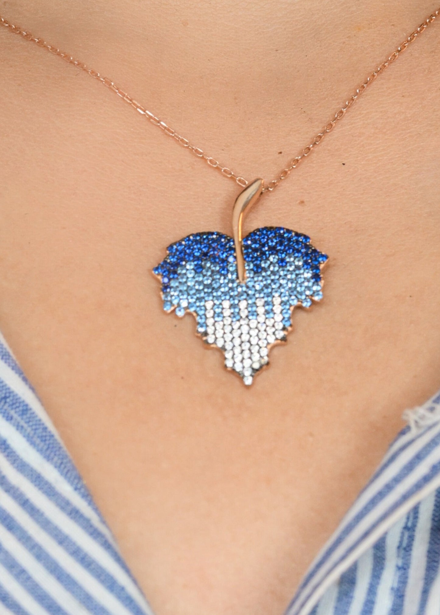 Heart-shaped blue pendant necklace on a person wearing a striped shirt