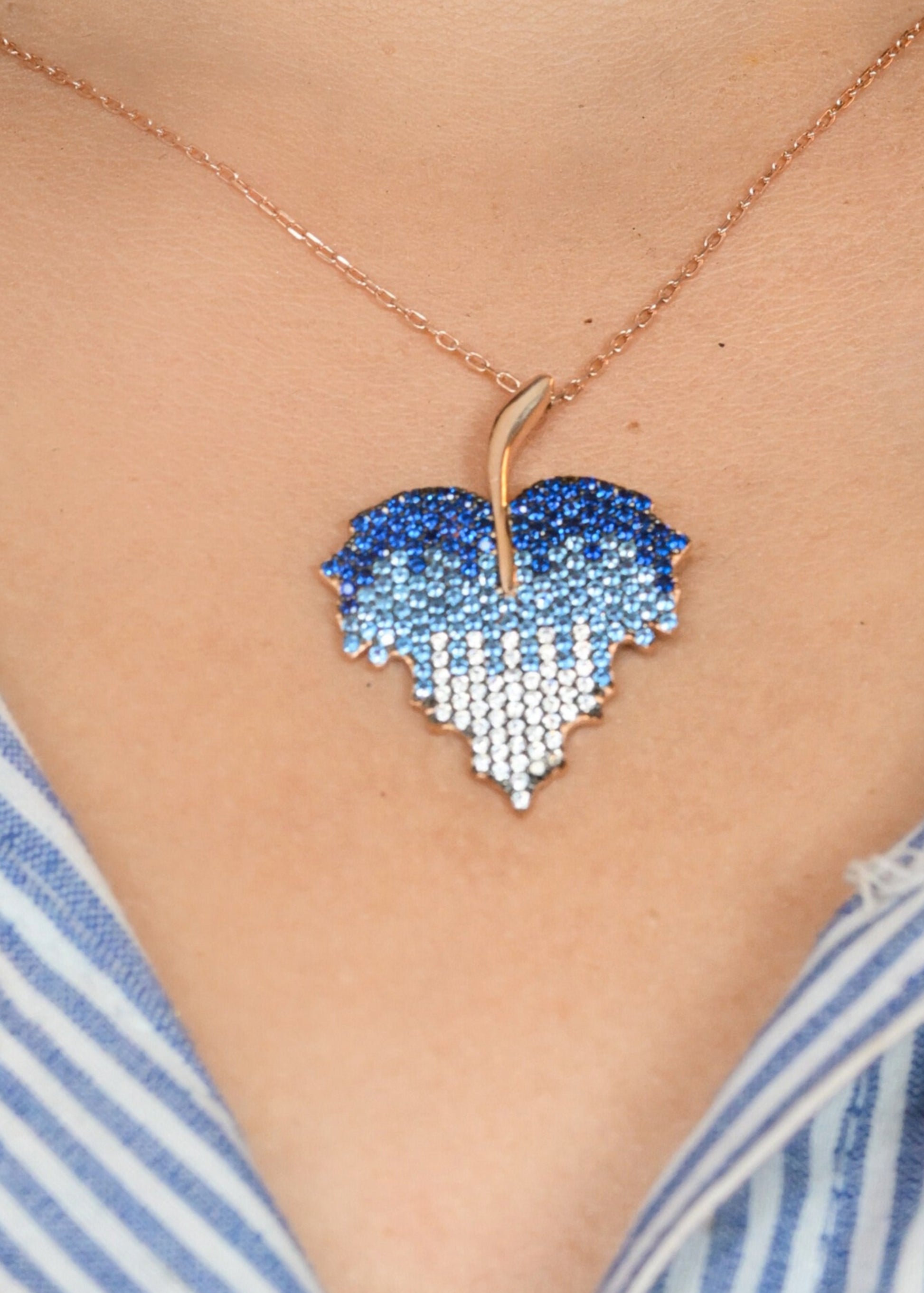 Heart-shaped blue pendant necklace on a person wearing a striped shirt