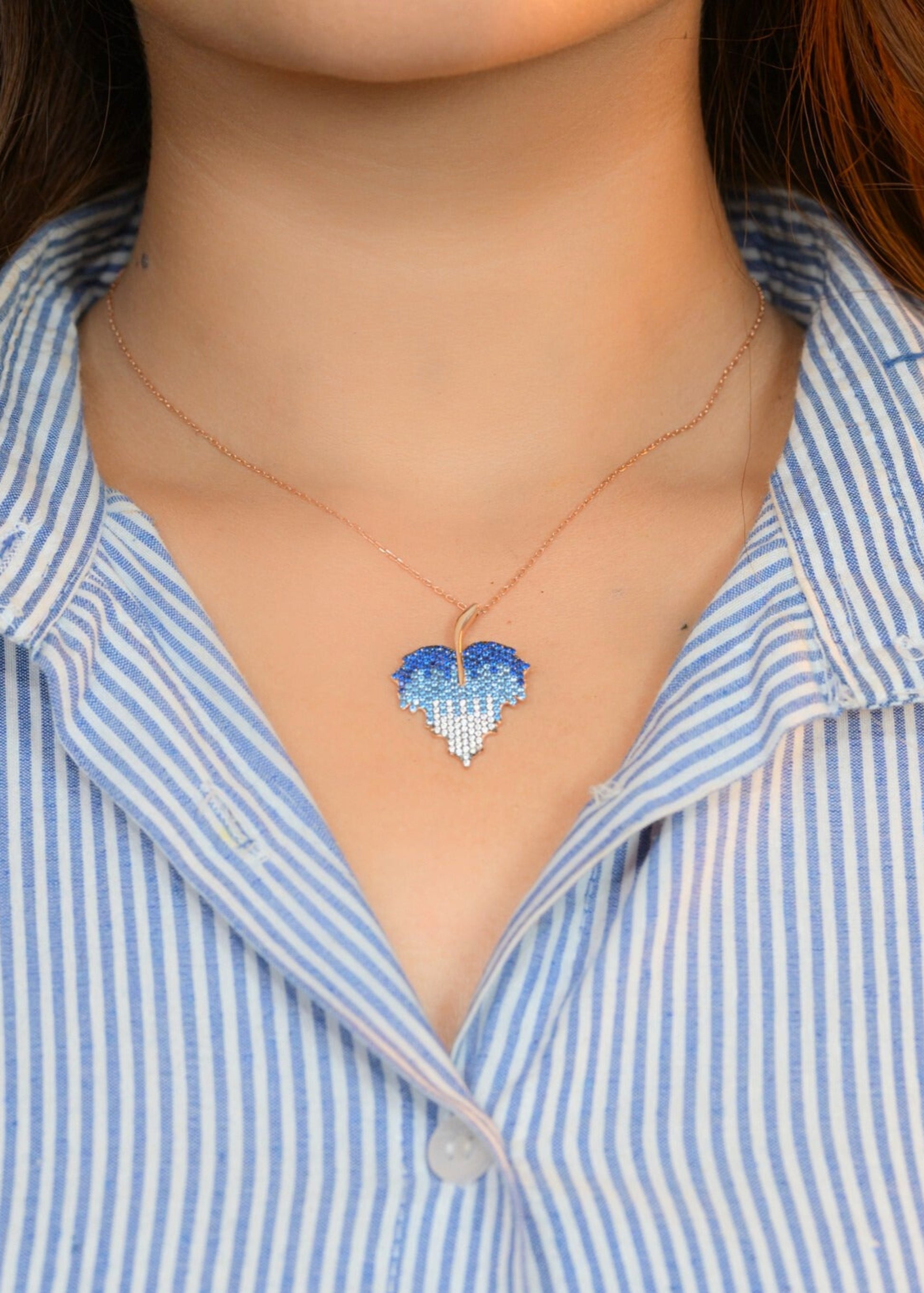 Person wearing a blue heart-shaped pendant necklace with a blue and white striped shirt.