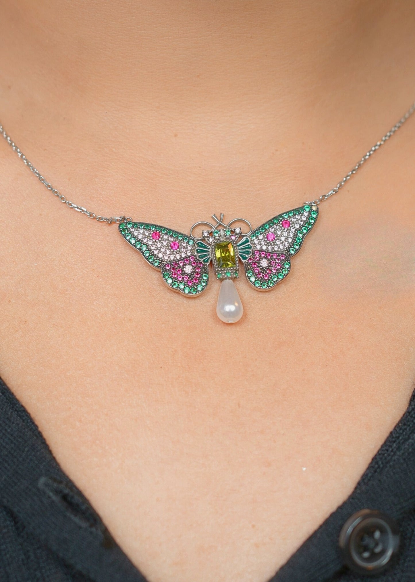 Butterfly necklace with gemstones and a pearl on a person's neck