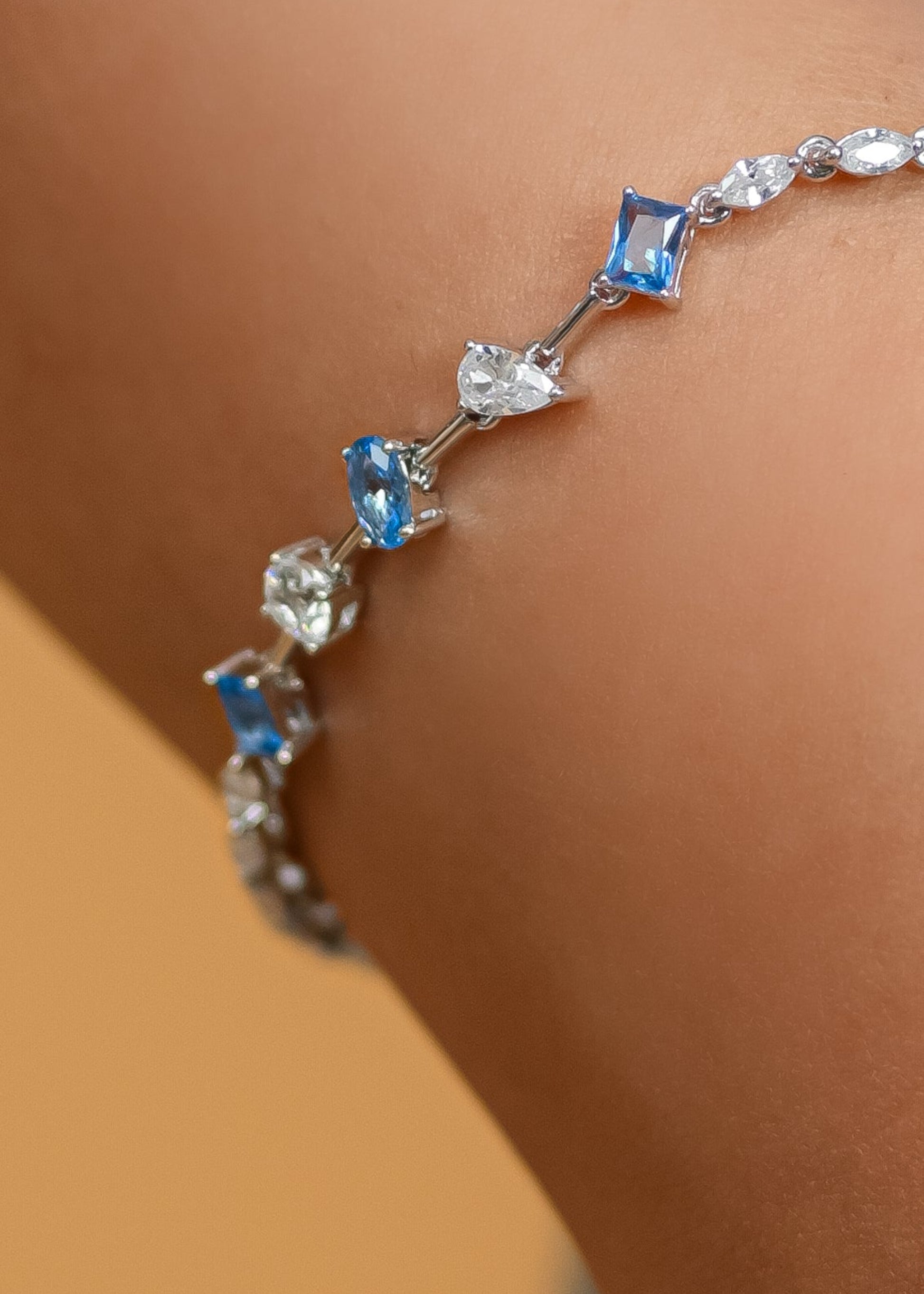 Silver bracelet with blue and clear gemstones on a wrist against a neutral background