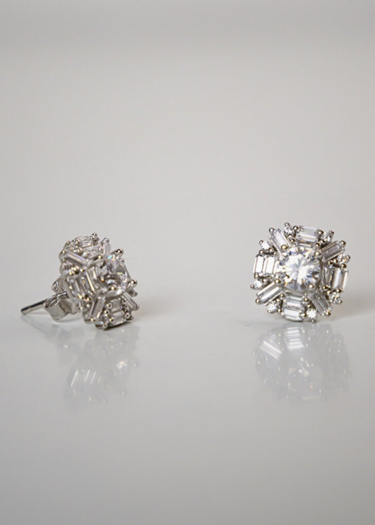 Pair of diamond stud earrings on a reflective surface with a light gray background