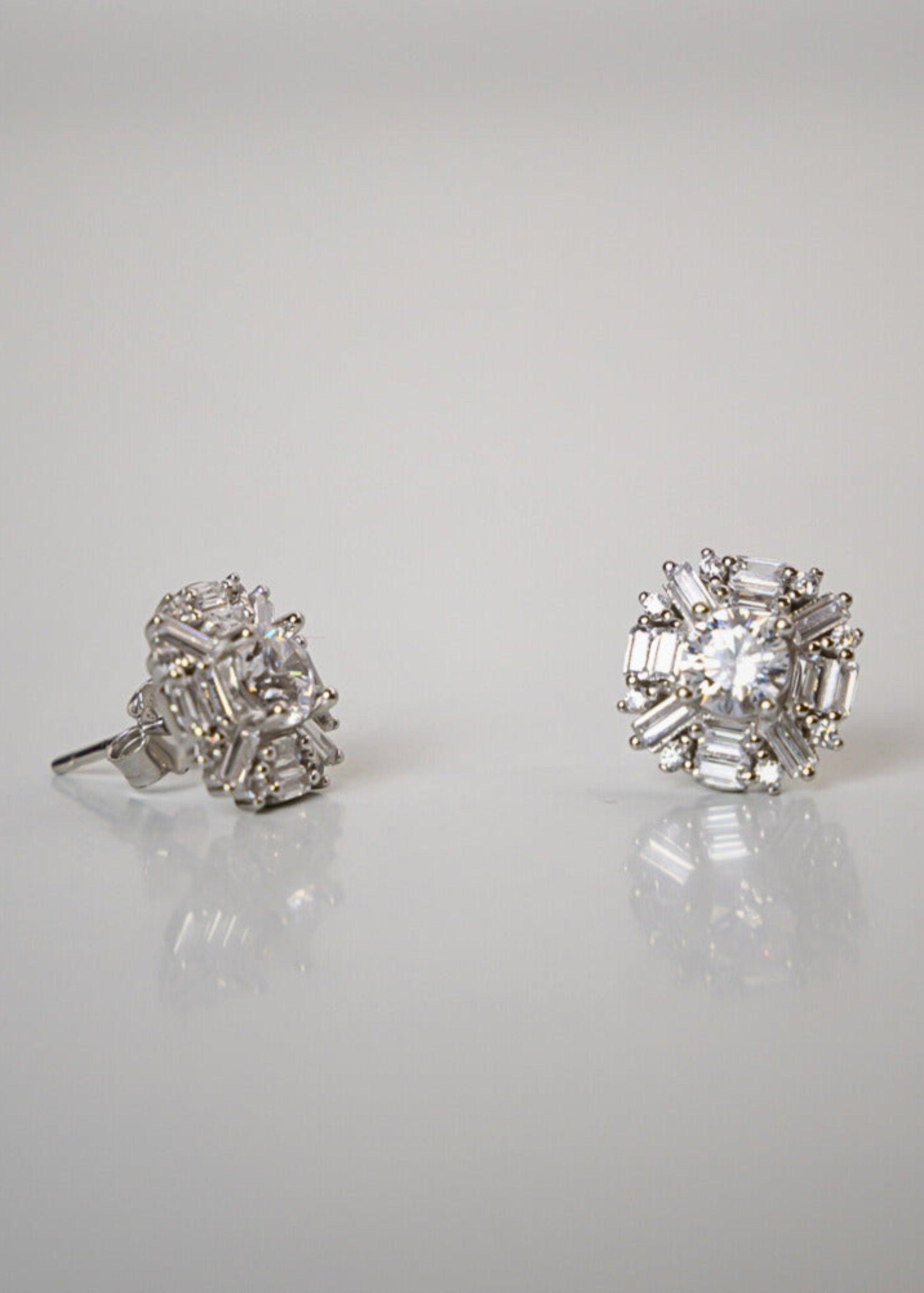 Pair of diamond stud earrings on a reflective surface with a light gray background