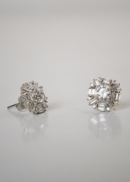 Pair of diamond stud earrings on a reflective surface with a light gray background