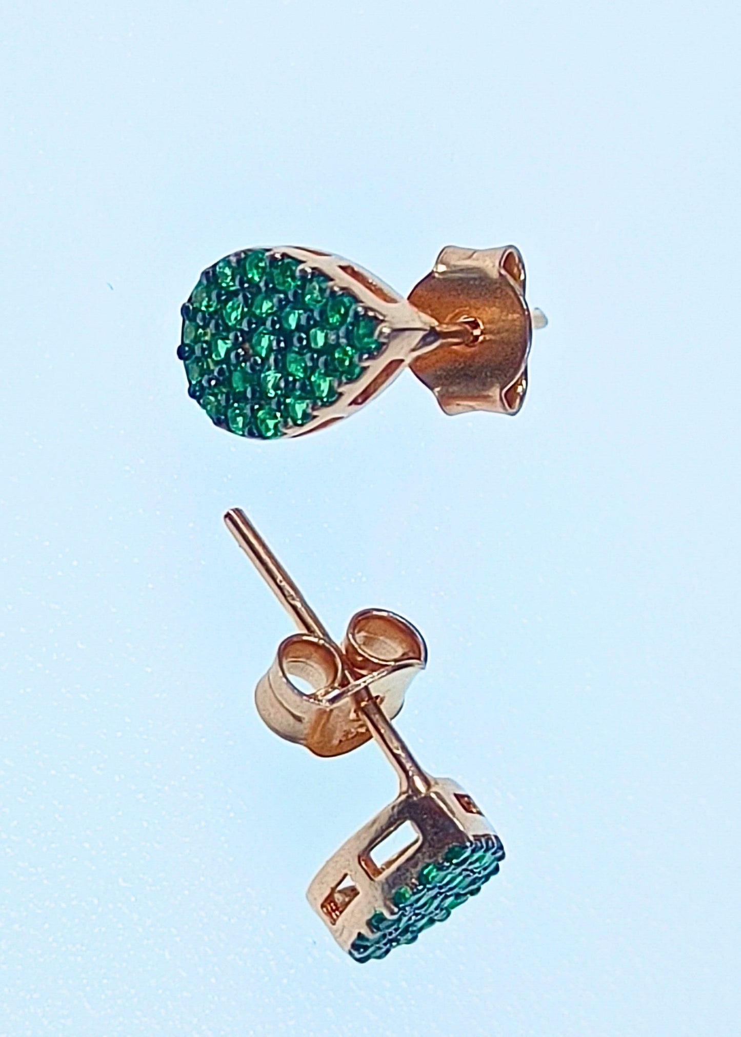 Rose gold earrings with green gemstones on a light blue background