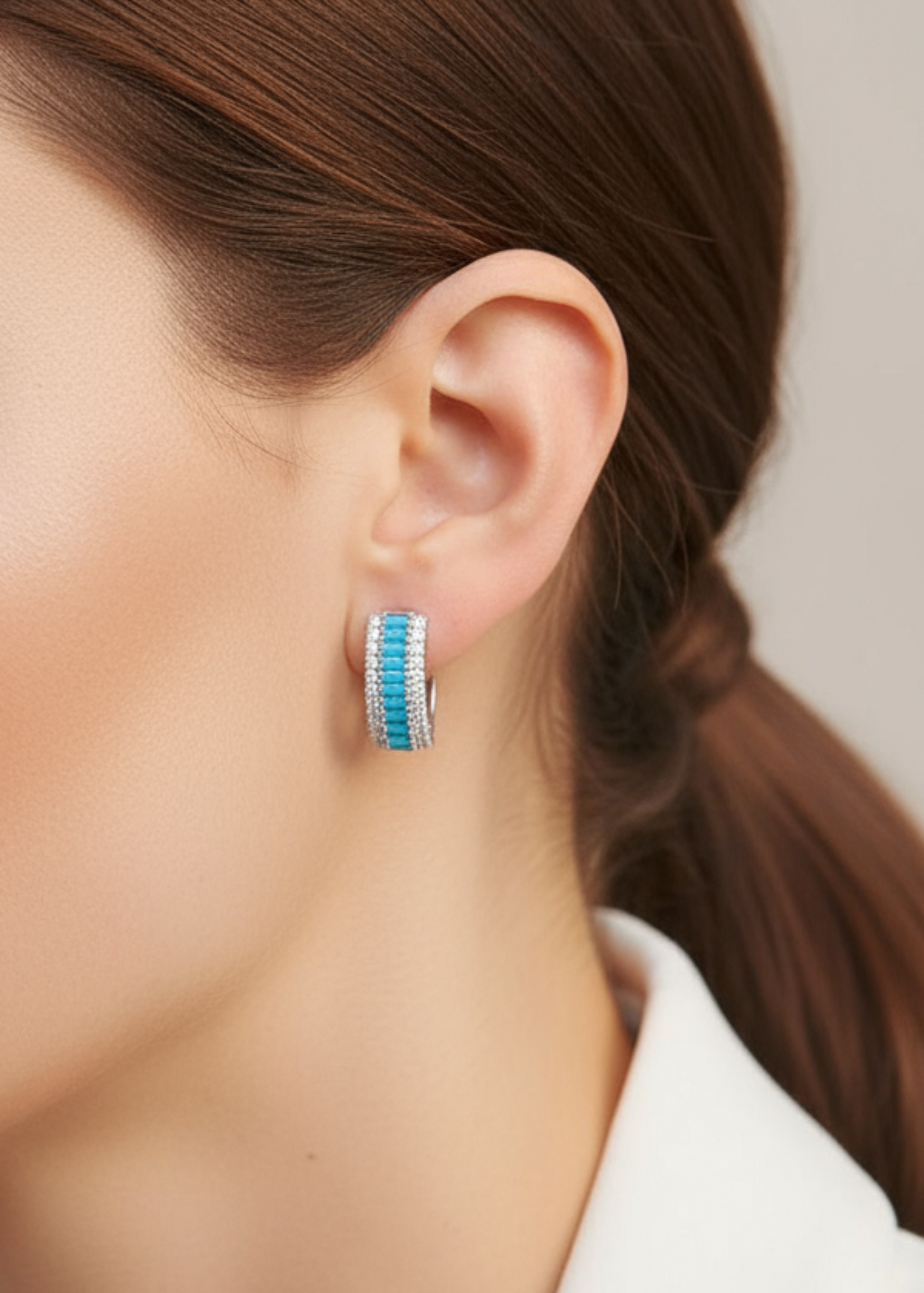 Close-up of a woman wearing a turquoise and silver earring against a neutral background